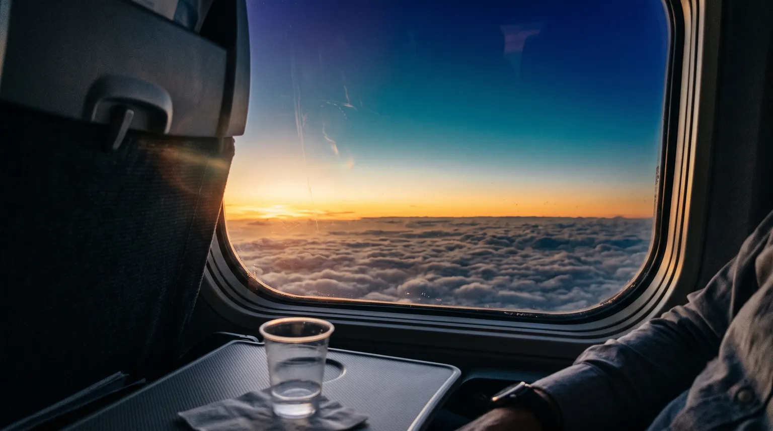 A traveller watching the sunset from an airplane window over the clouds.