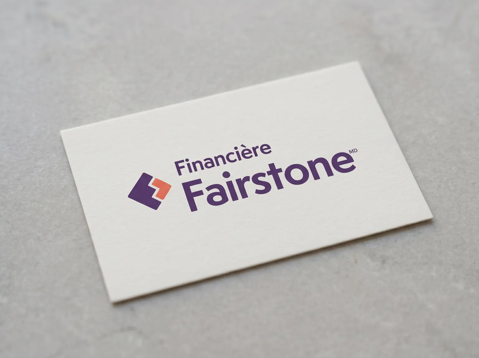 Le logo de Financière Fairstone sur une carte unie posée sur une surface de pierre pâle, sous une douce lumière du jour.