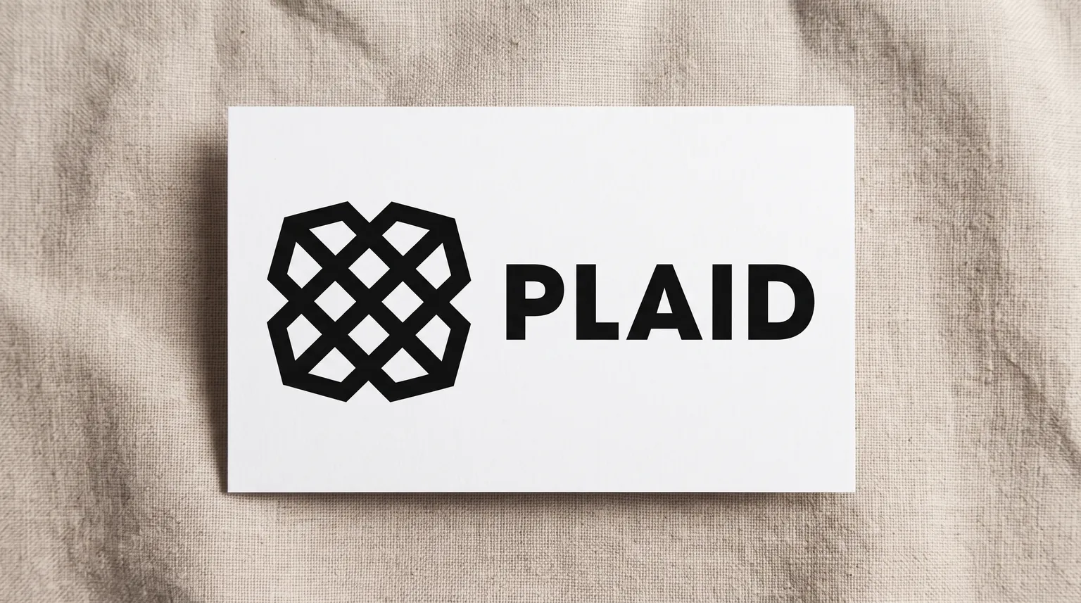 The Plaid logo on a matte white card resting on a piece of warm natural linen.