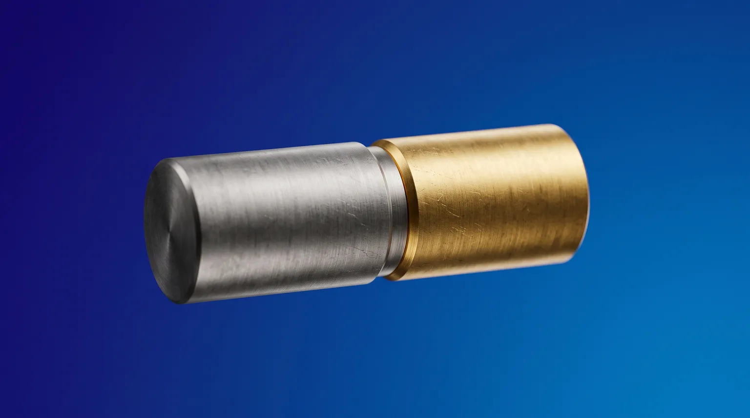 Un cylindre d'acier brossé et un cylindre de laiton joints bout à bout, un anneau doré à la jonction, sur fond bleu.