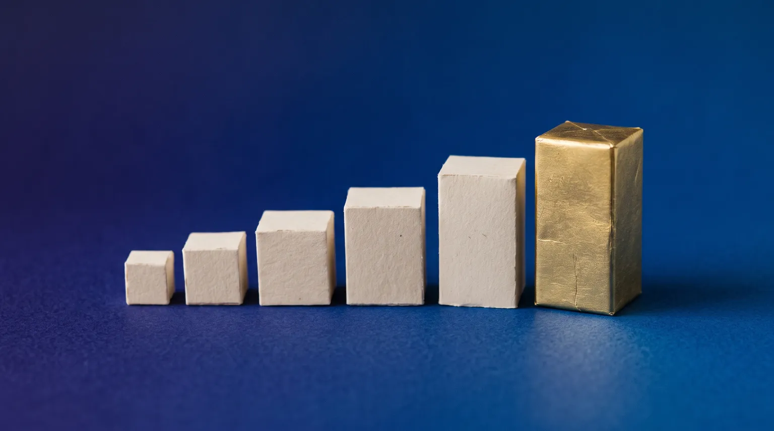 Small paper blocks rising in a row on a deep blue ground, the tallest one in gold foil.