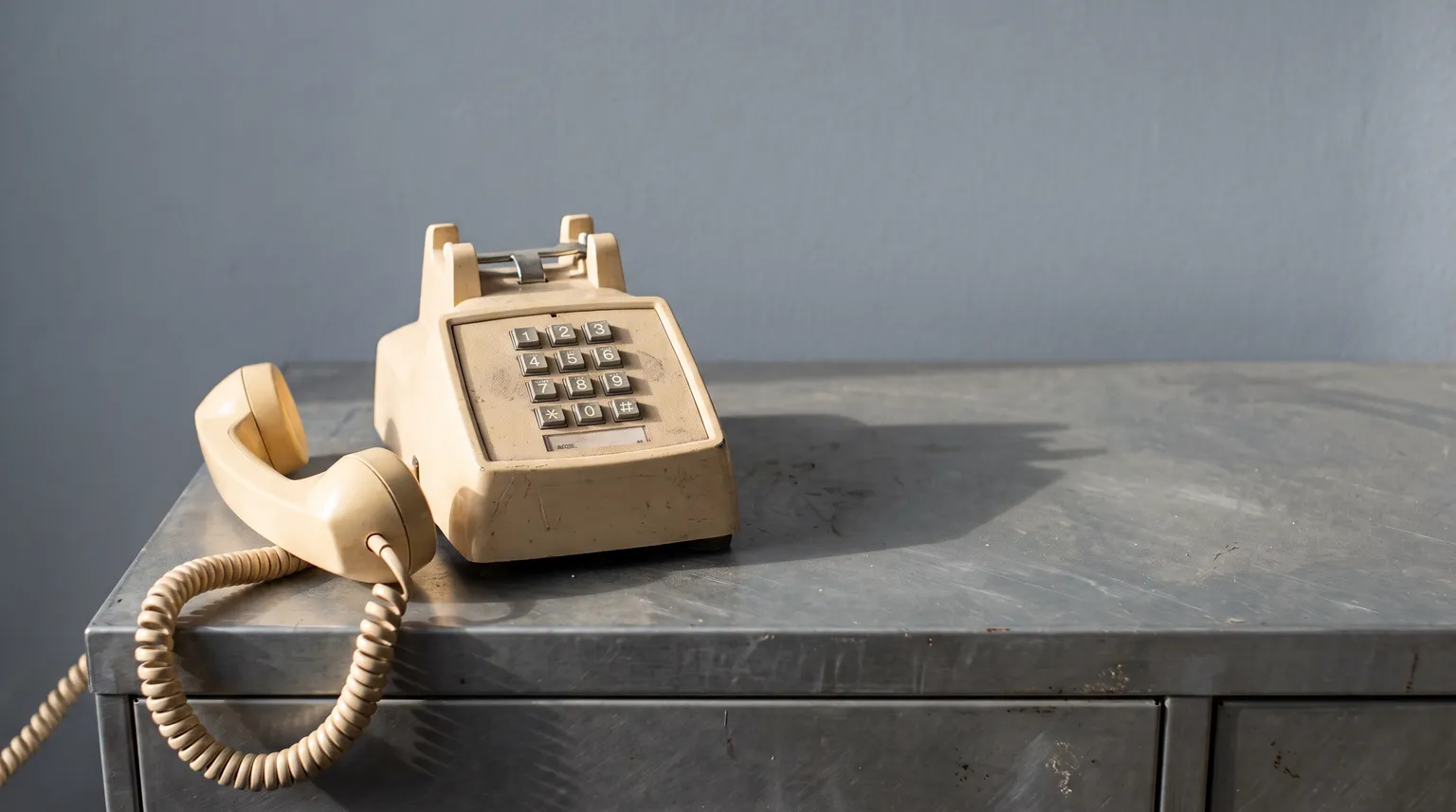 Un téléphone de bureau décroché sur un classeur gris, le combiné posé à côté.