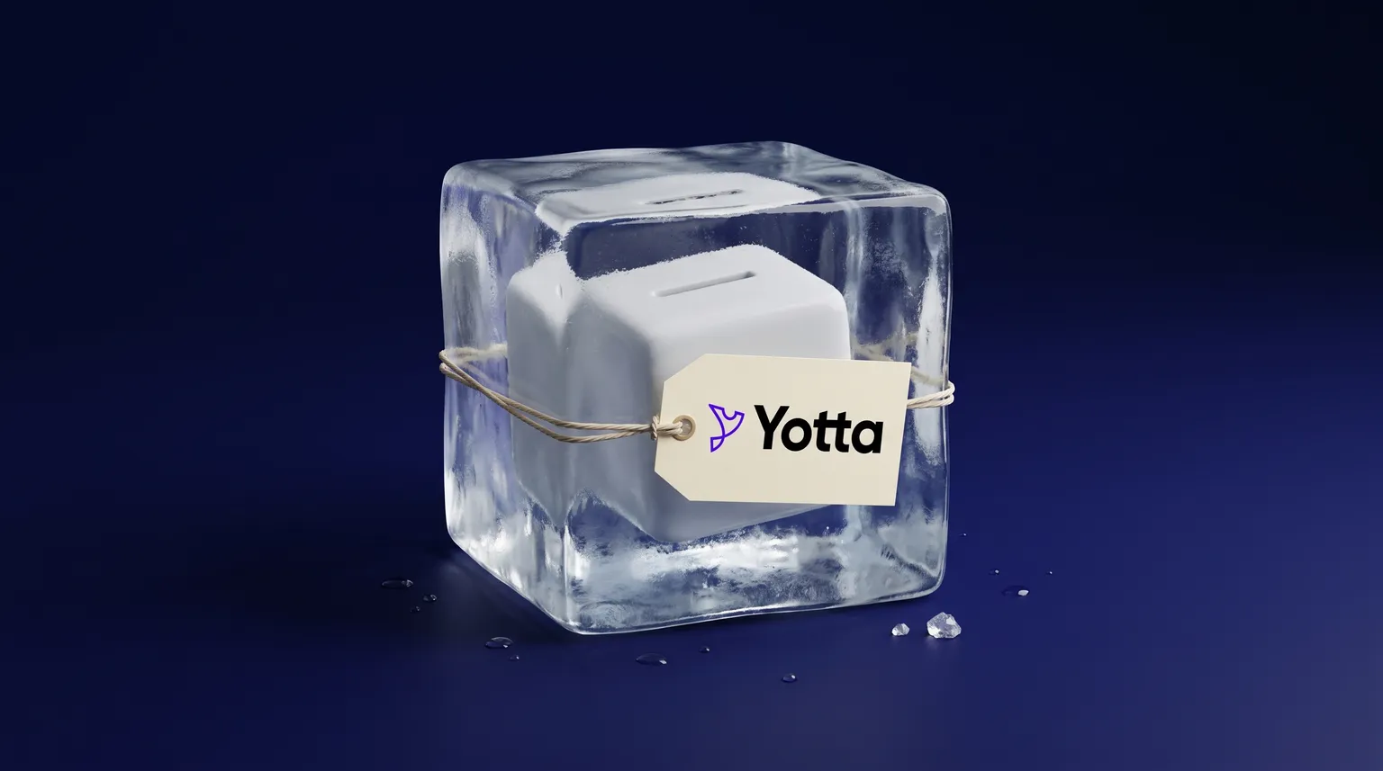 A white coin bank frozen inside a clear block of ice, with a paper tag showing the Yotta logo tied around the block, on a dark blue backdrop.