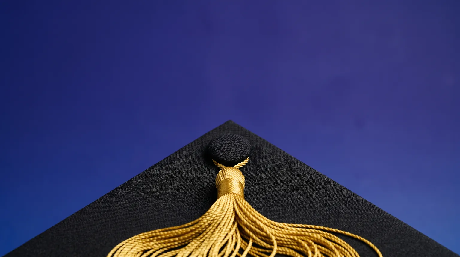 A graduation cap photographed close up on a blue gradient background, its tassel cord in gold.