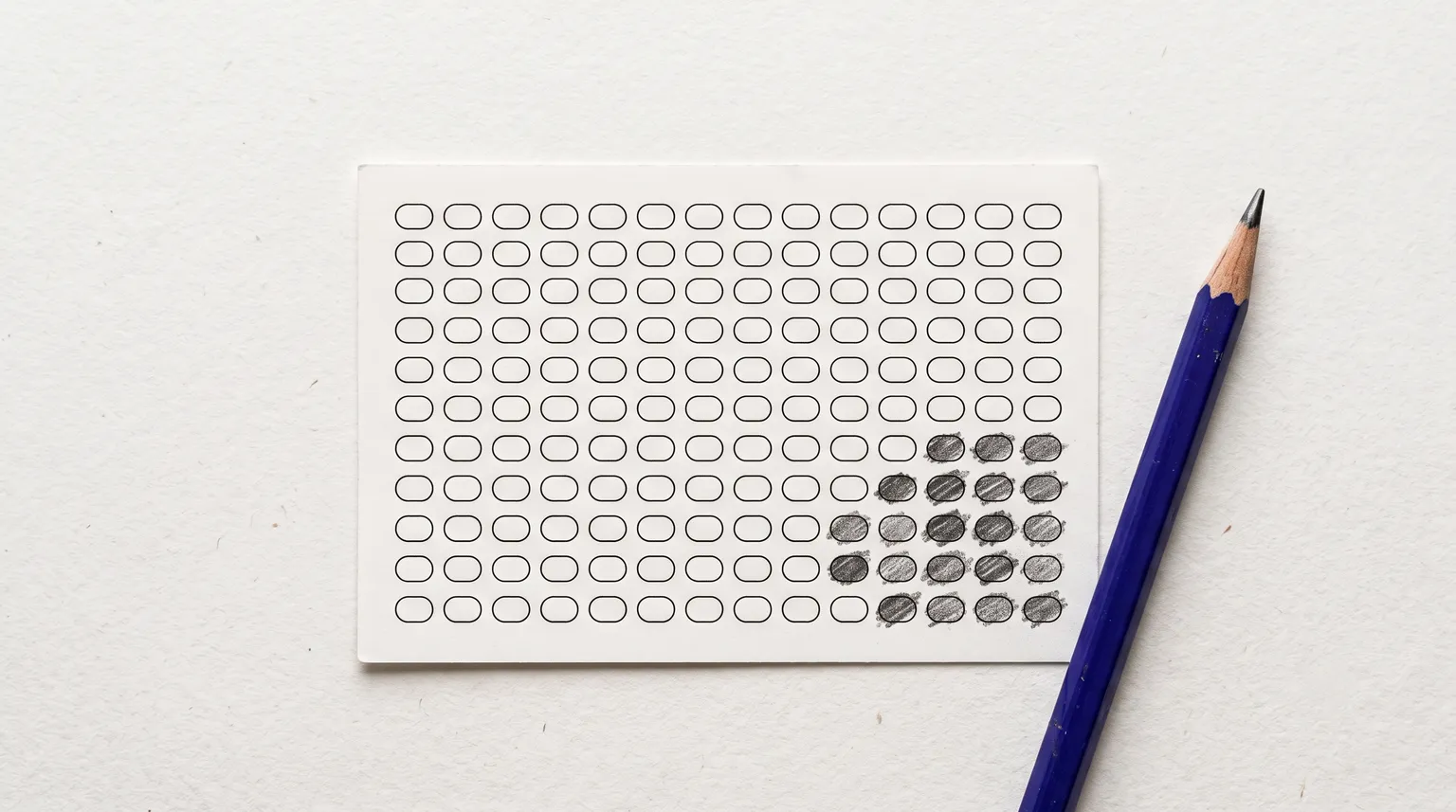 Une fiche de loterie avec des cases remplies au crayon regroupées dans un coin, un crayon bleu à côté.